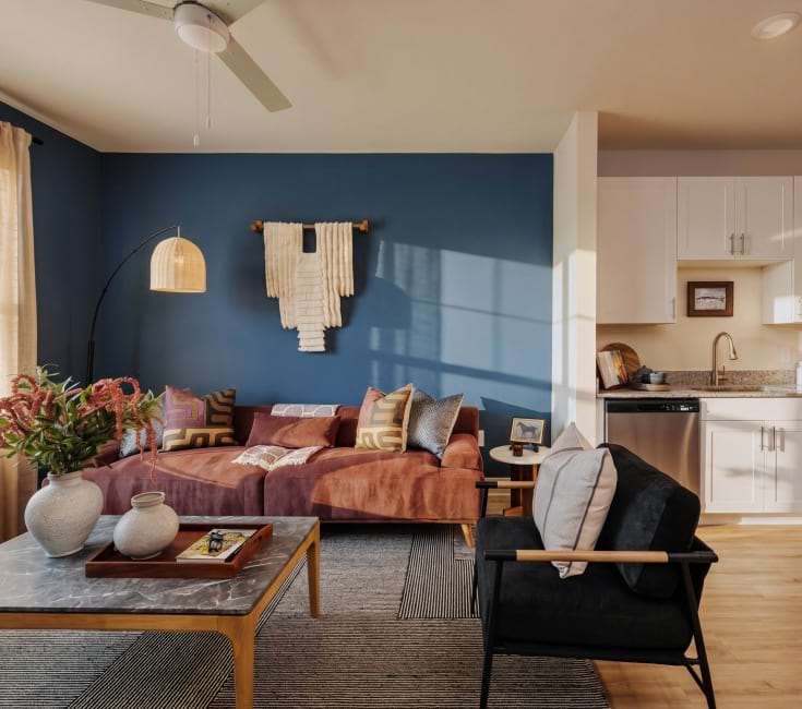 Living room with modern decor and natural sunlight, open to kitchen with stainless steel appliances, white cabinetry and wood-look flooring Living room with modern decor and natural sunlight, open to kitchen with stainless steel appliances, white cabinetry and wood-look flooring